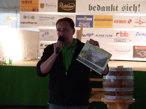 Redner mit Mikrofon und Kalender vor Sponsor-Tafel