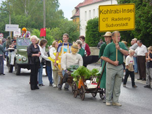 Festzug mit Mitgliedern des Vereins und gelbem Ortsschild