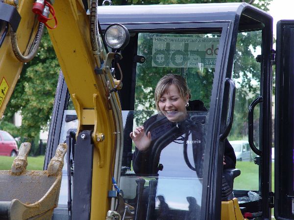 Lächelnde Frau winkt aus dem Führerhaus eines gelben Baggers