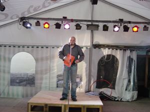 Mann steht auf kleiner Bühne im Zelt vor Publikum