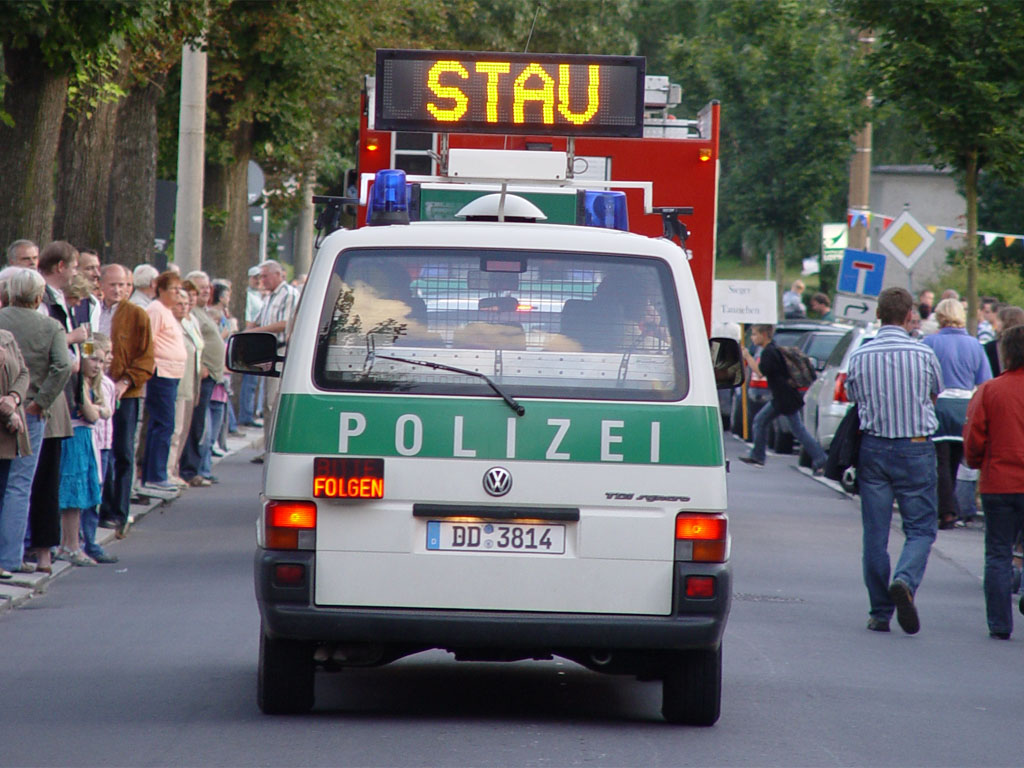 Polizeiwagen mit Blaulicht auf einer Straße während eines Festzugs