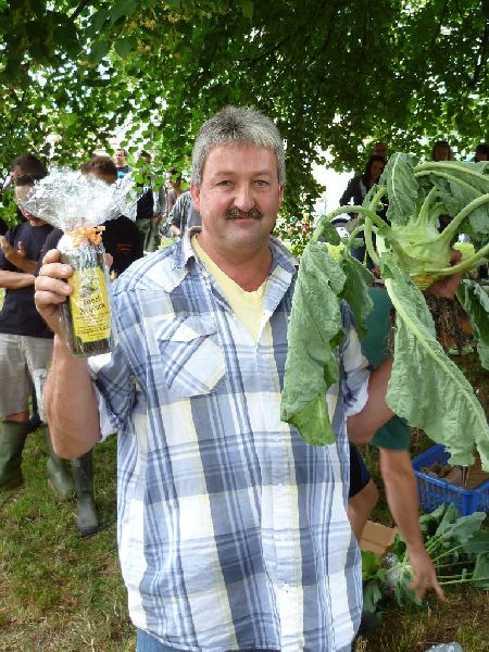 Mann hält Kohlrabi und Flasche unter Bäumen